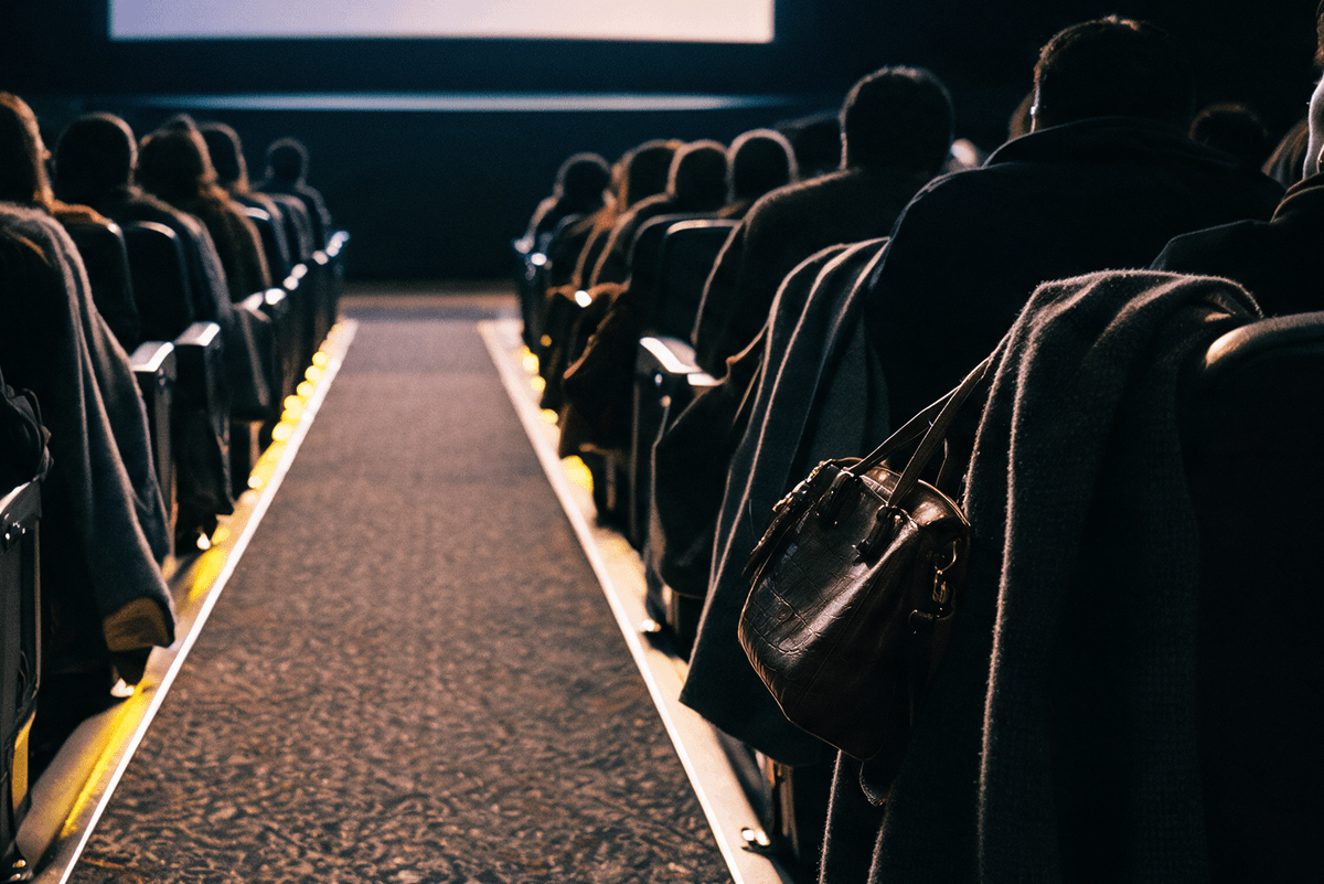 Brown purse and winter coat draped over the back of a movie theater seat in a dimly lit auditorium.