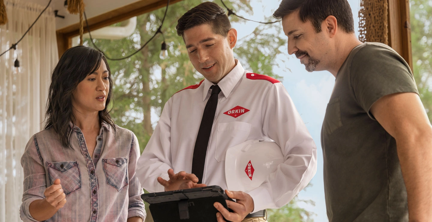 An Orkin Pro speaking about pest control services with a couple on their balcony