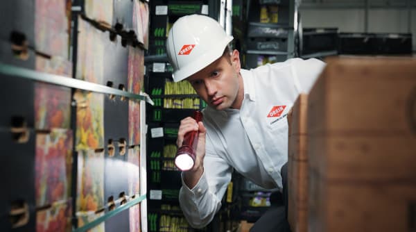 A Commercial Orkin Pro holding a flashlight performing an inspection of a commercial stored product warehouse