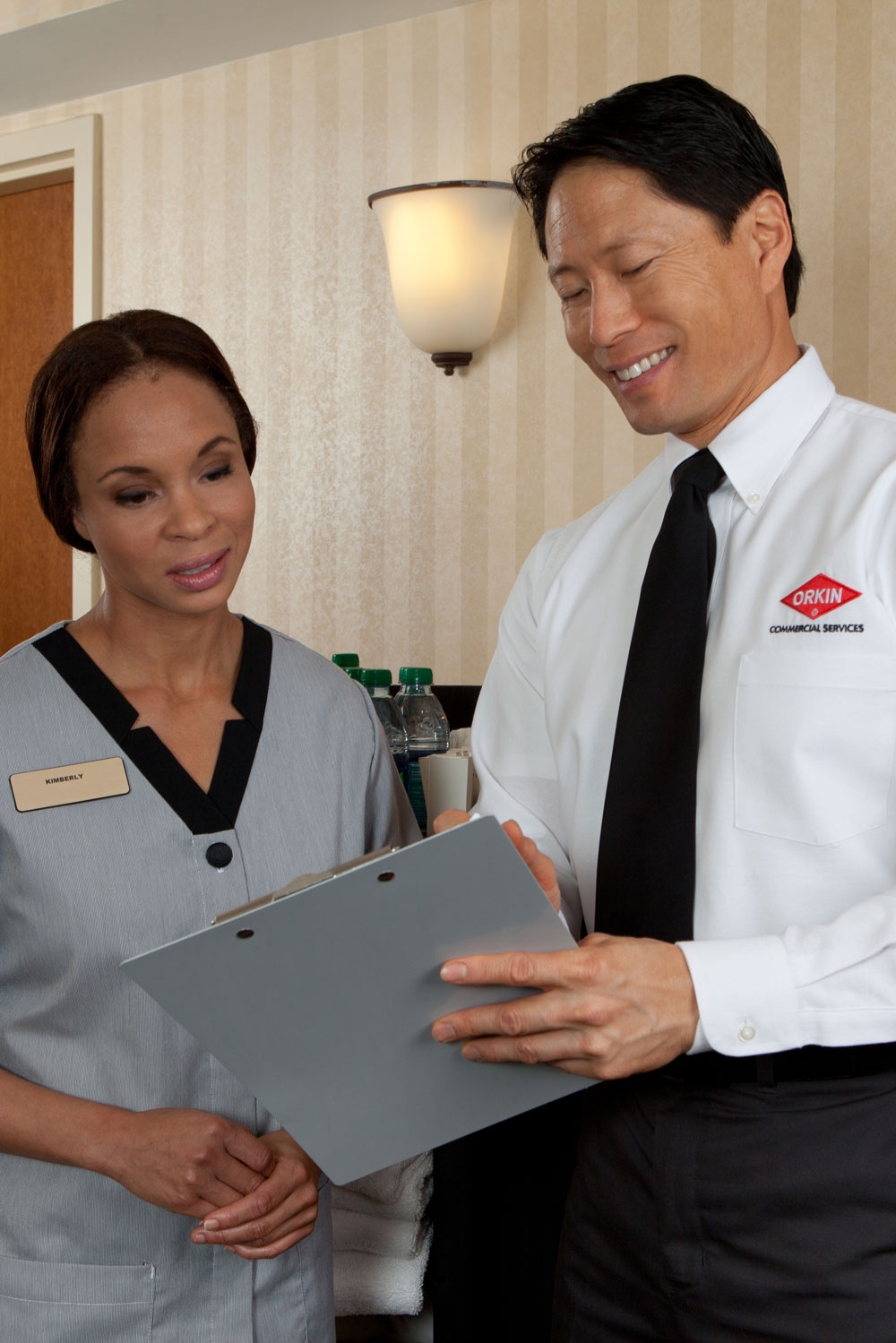 An Orkin Pro looking at a clipboard with a client in a hotel room