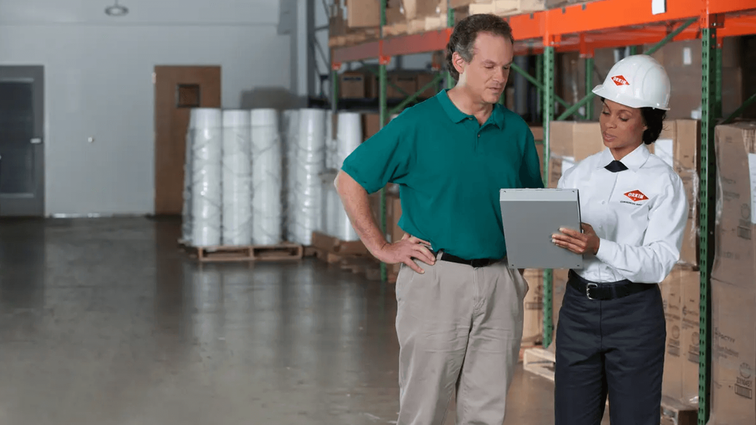 Food processing facility professional standing in a warehouse with an Orkin commercial pest treatment professional, reviewing findings from a pest control program.